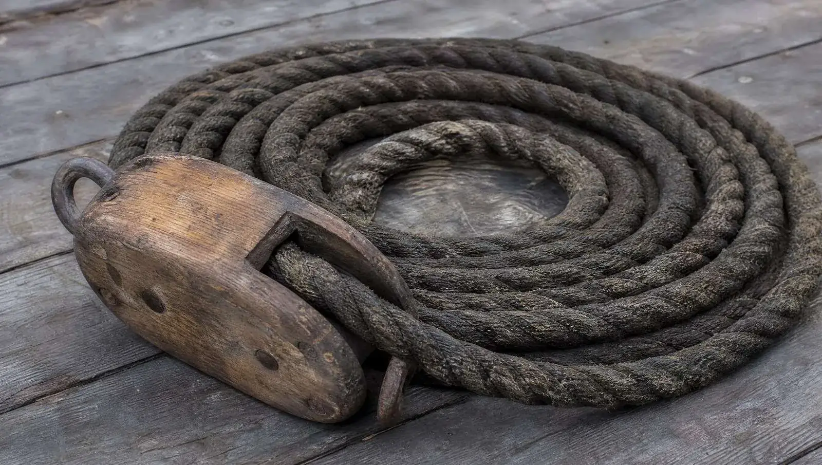 A coil of tarred hemp rope and a wooden pulley block on deck planking